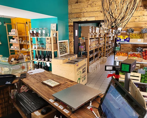 Une personne prenant l'ensemble du magasin depuis la caisse. On retrouve en arrière-plan les produits alimentaires, les boissons et les différents produits vrac
